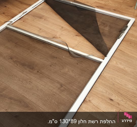 מסגרת חלון עם רשת קרועה על רצפת עץ